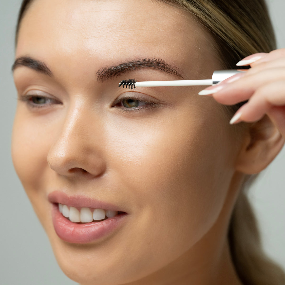 Woman applying brow growth serum with a neutral background