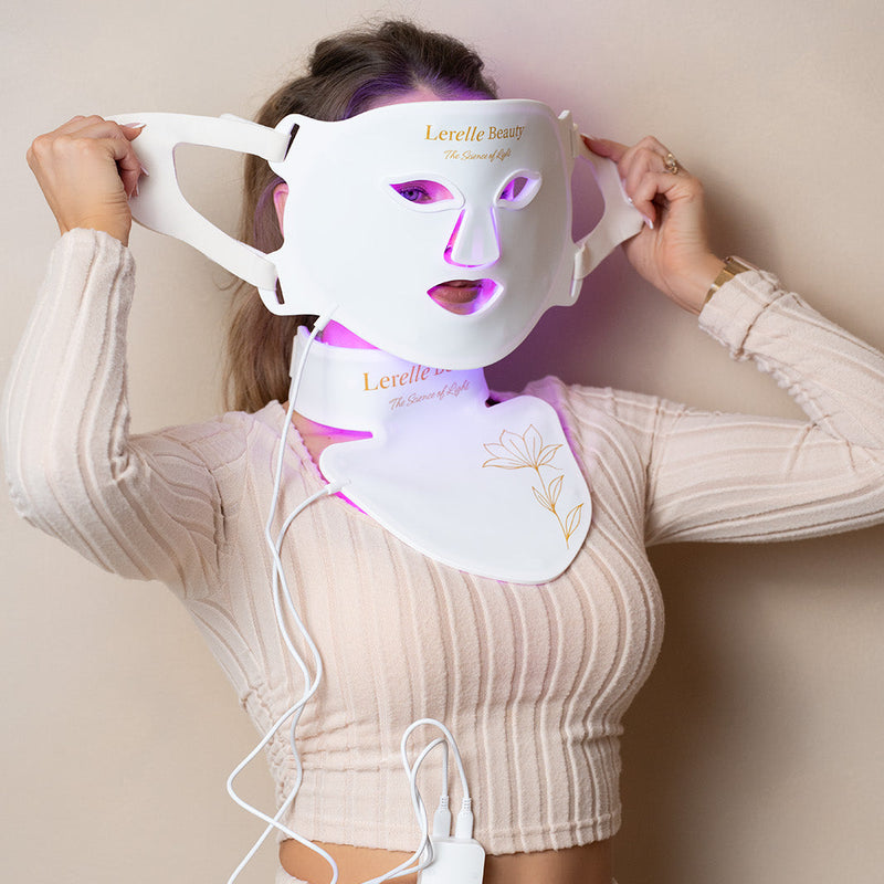 Person wearing a LED face and neck mask with visible branding on a plain background
