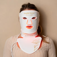 Person wearing a white LED face and neck mask with visible branding on a beige background
