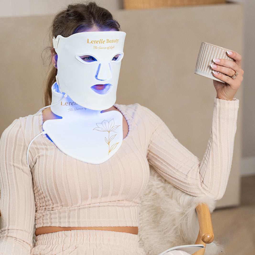 Person wearing a LED face and neck mask while sitting on a couch.